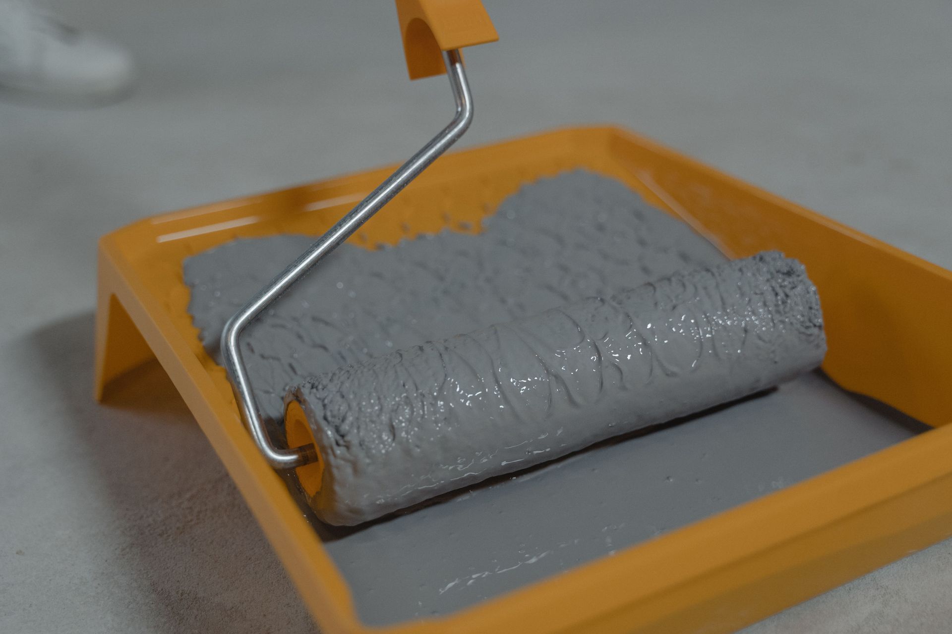 Detailed view of a gray paint roller placed in an orange tray, ready for painting.